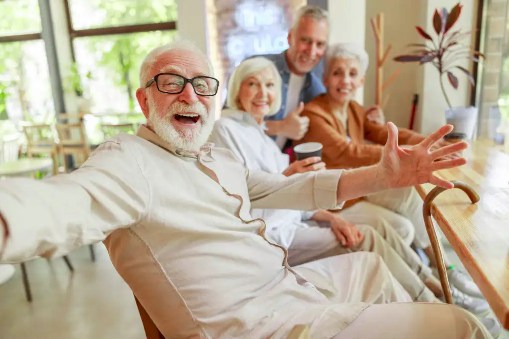 Four old people sit indoors, smiling at the camera.