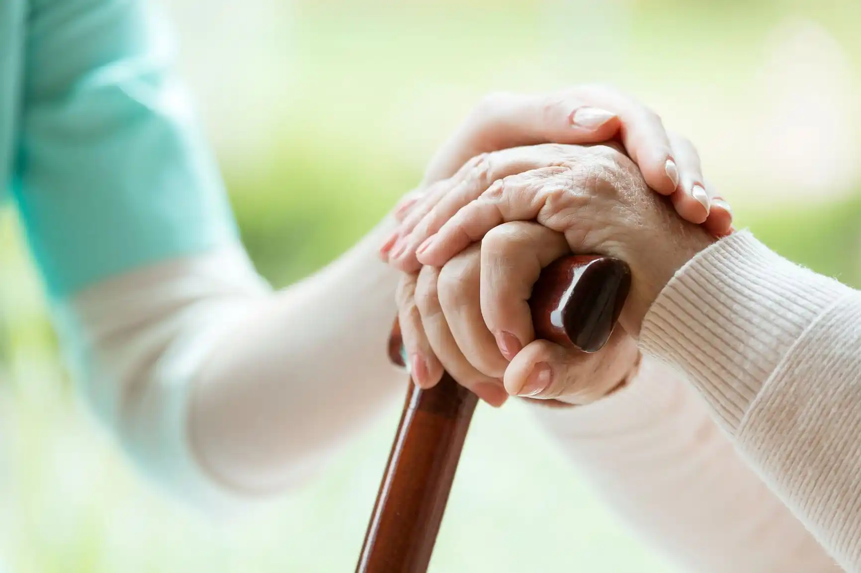 A nurse holds the hand of an elderly woman, who is holding a walking stick.